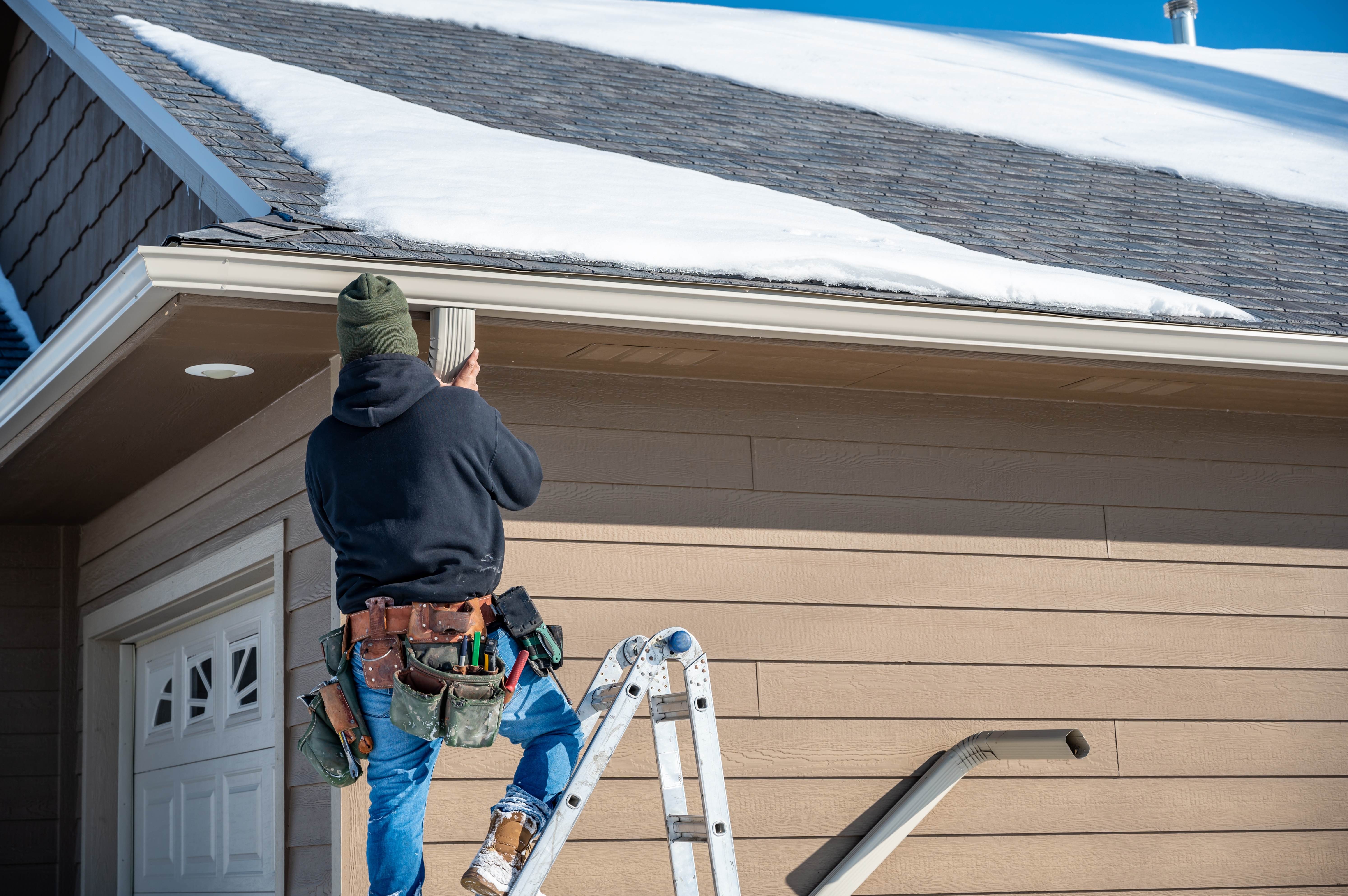 man installing gutter downspout in winter